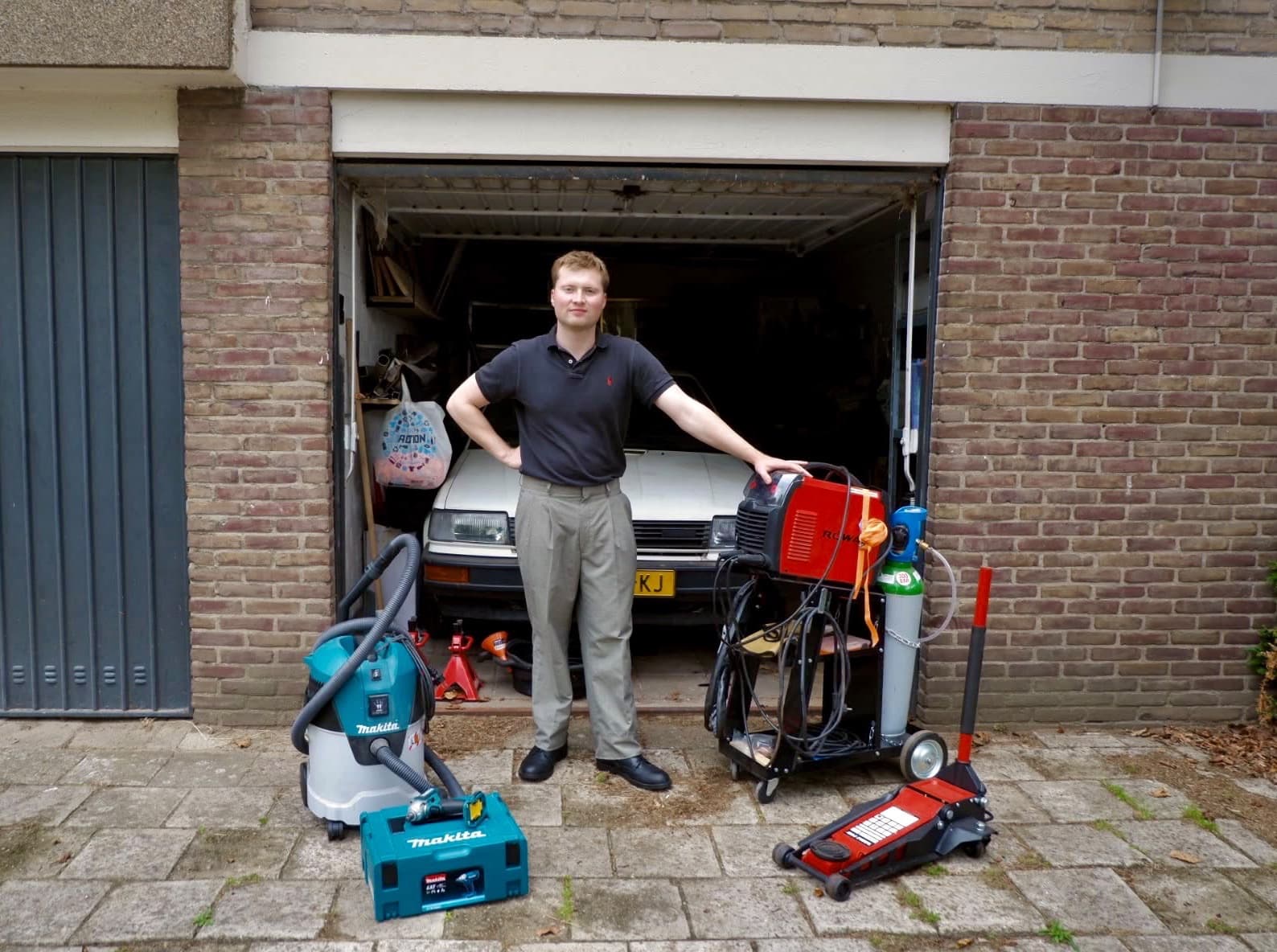 Iemand voor zijn garagebox, met gereedschap en een krik op de oprit
